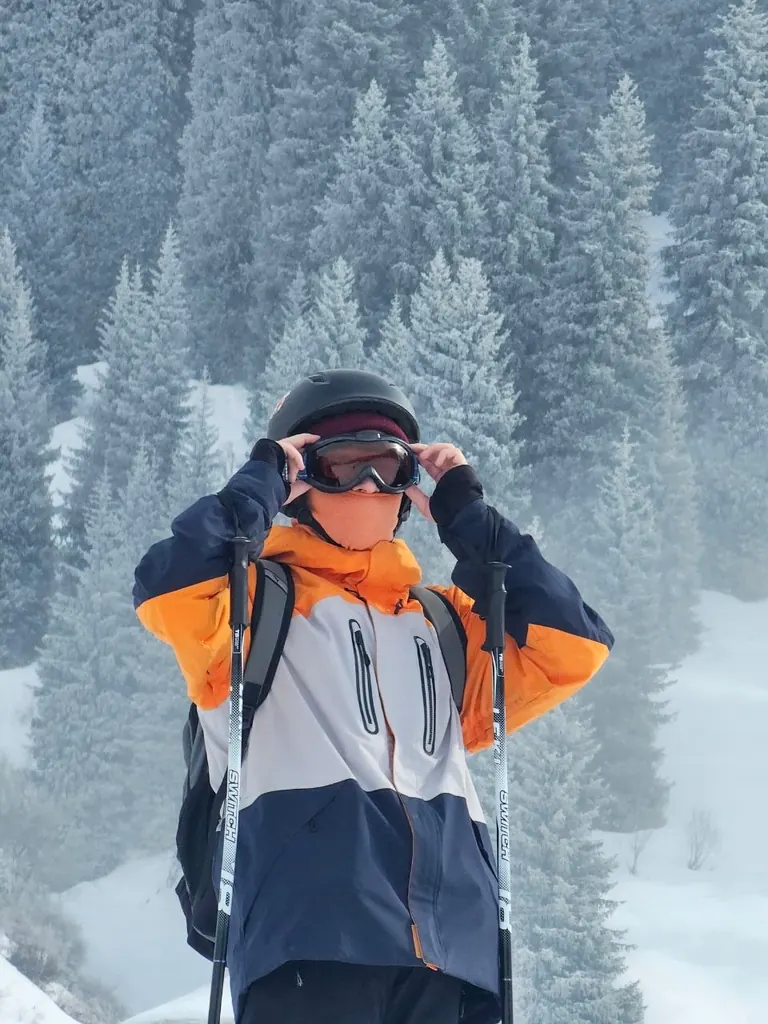 Yakov in ski gear adjusting his goggles among snowy fir trees